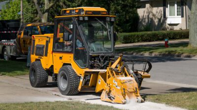 Trackless MT7 sidewalk tractor with cold planer attachment grinding sidewalk