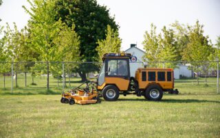 Yellow Trackless MT7 tractor and lawn mower attachment mowing campus grass