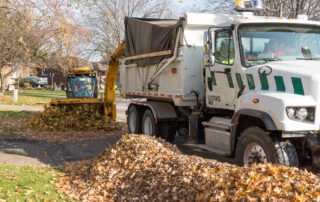 trackless leaf loader performing leaf cleanup and leaf collection on a municipality's street in autumn