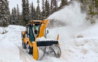 Yellow trackless MT7 municipal tractor and ribbon snowblower blowing snow