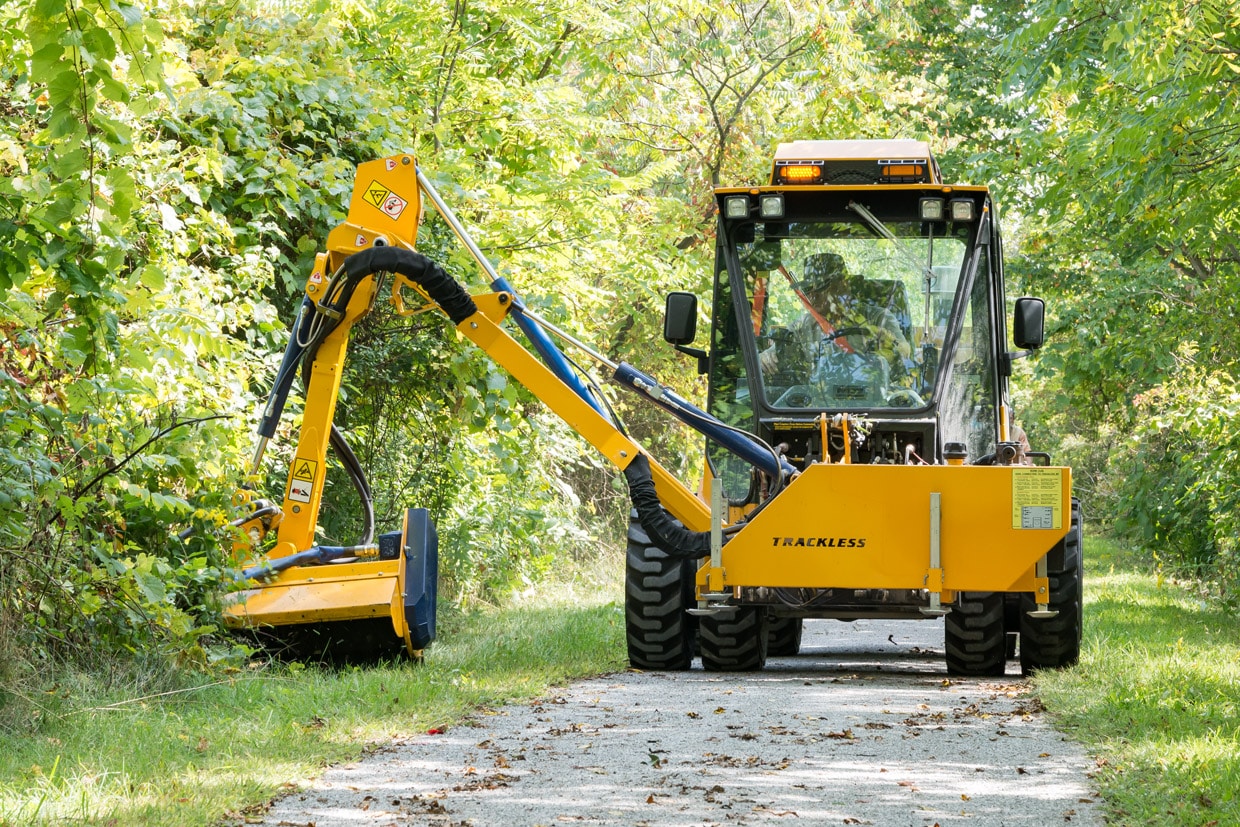 trackless vehicles boom flail mower attachment on sidewalk municipal tractor mowing grass in ditch front view