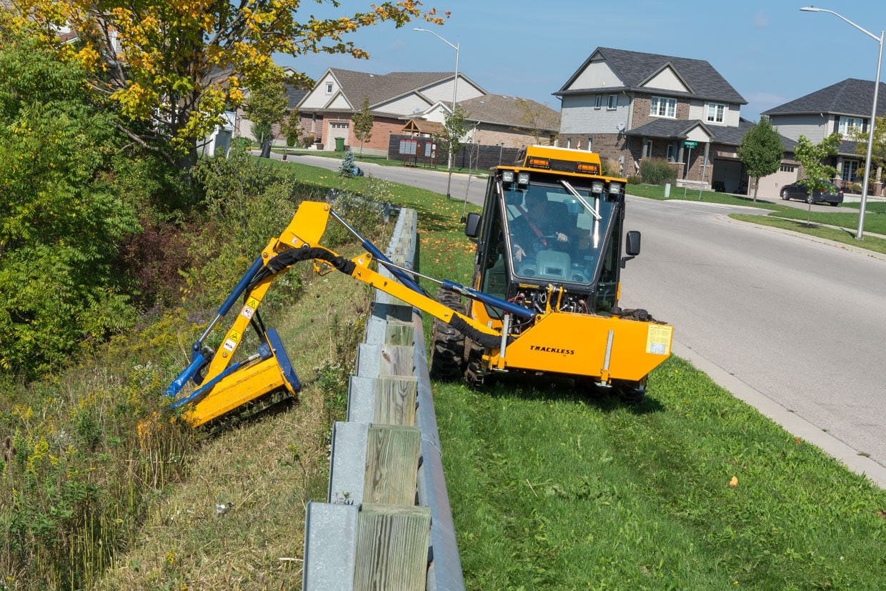 trackless vehicles boom flail mower attachment on sidewalk municipal tractor mowing grass in ditch front view