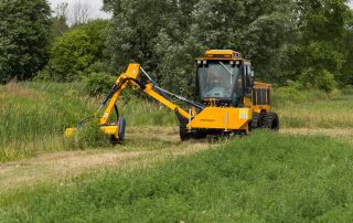 trackless vehicles boom flail mower attachment on sidewalk municipal tractor mowing grass front view