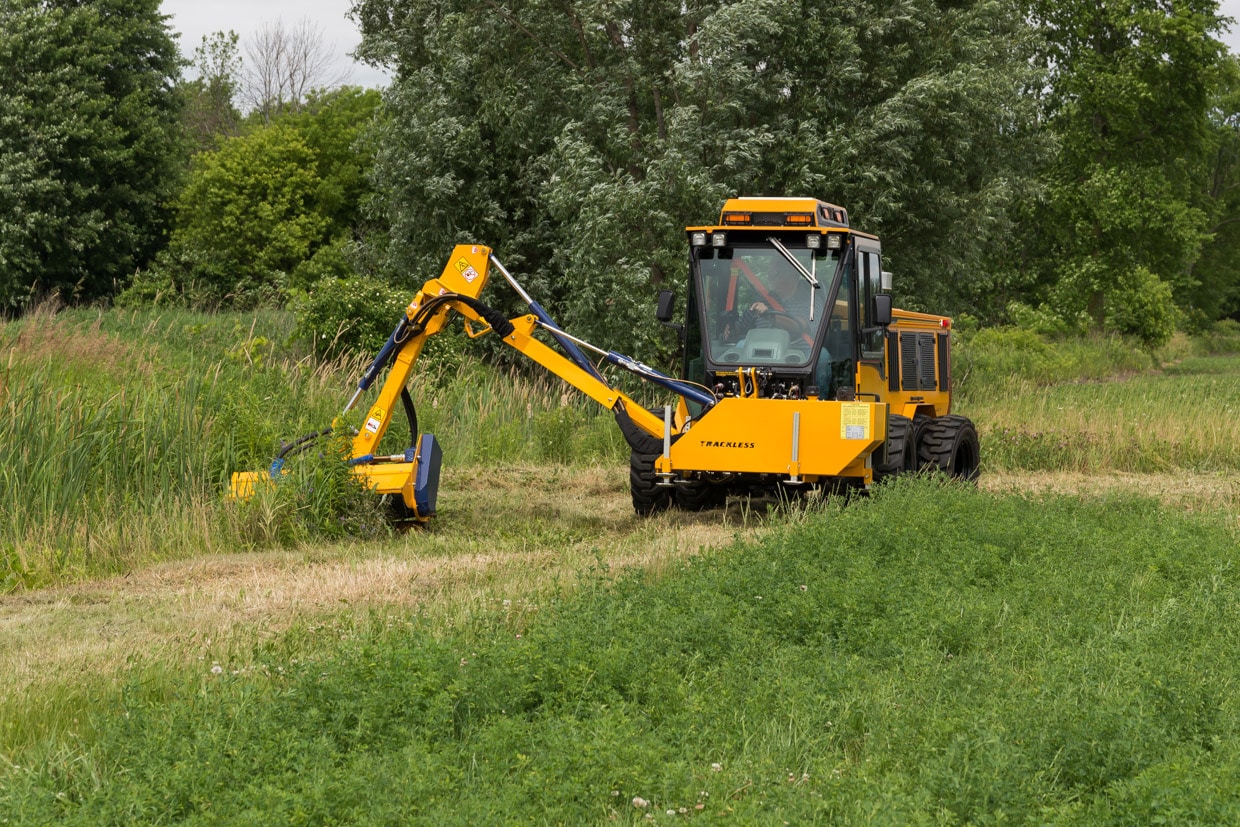 trackless vehicles boom flail mower attachment on sidewalk municipal tractor mowing grass front view