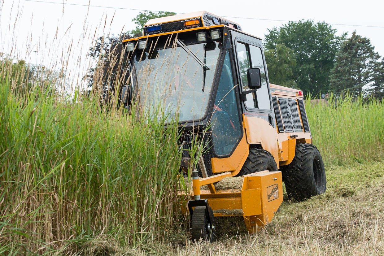 trackless vehicles front flail mower attachment on sidewalk municipal tractor mowing grass side front view