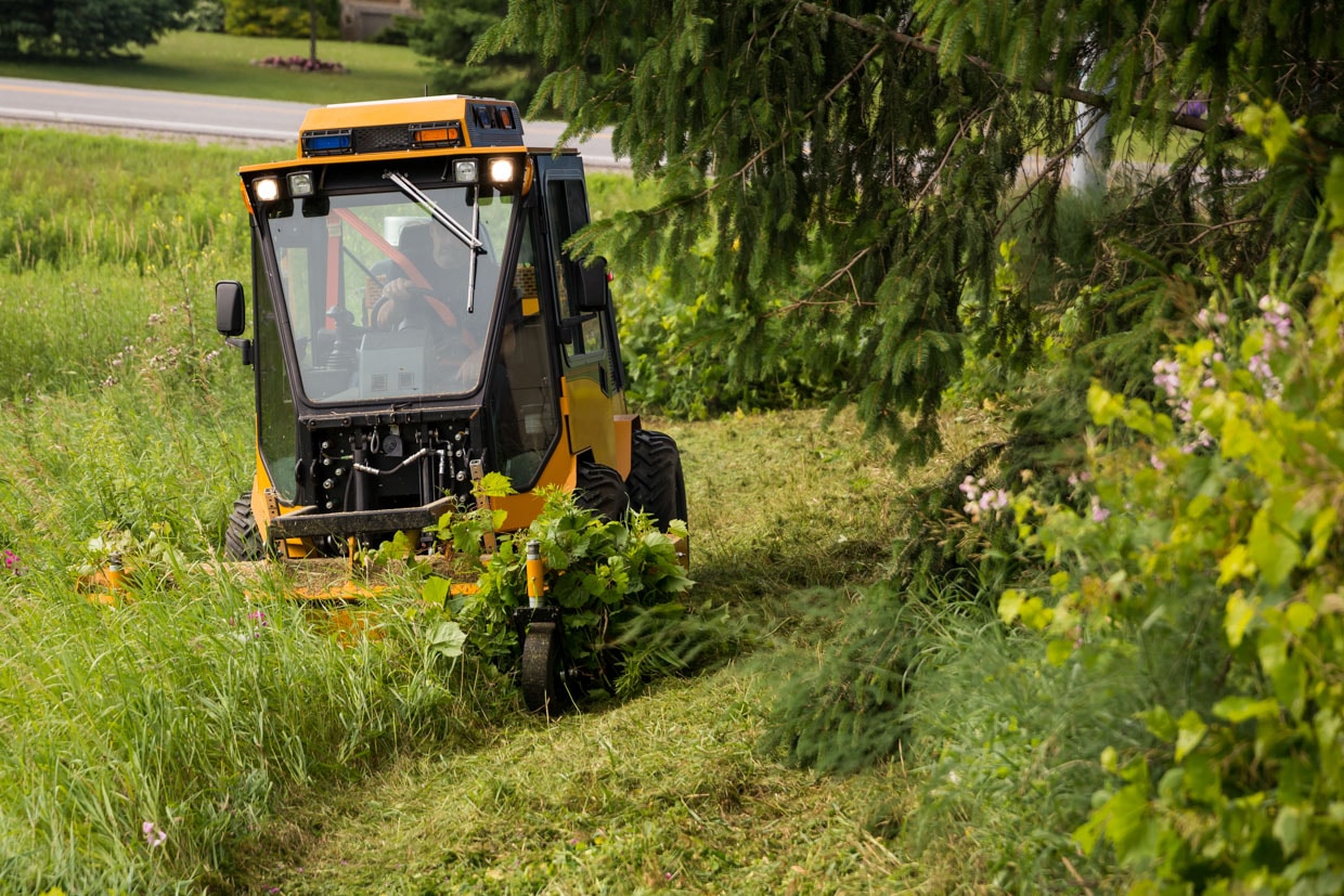 trackless vehicles front flail mower attachment on sidewalk municipal tractor mowing grass front view