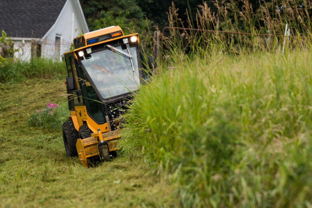 trackless vehicles front flail mower attachment on sidewalk municipal tractor mowing grass front view