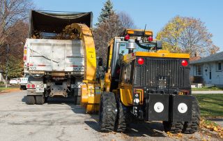 trackless vehicles leaf loader attachment on sidewalk municipal tractor loading leaves rear view