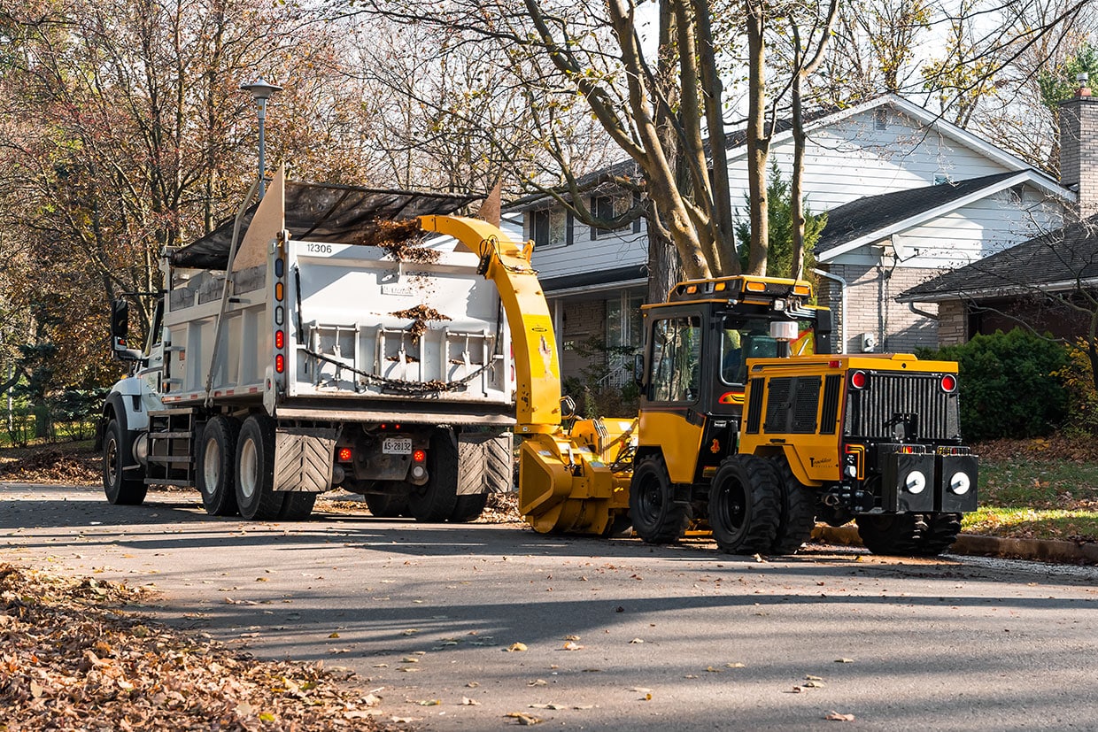 trackless vehicles leaf loader attachment on sidewalk municipal tractor loading leaves rear side view