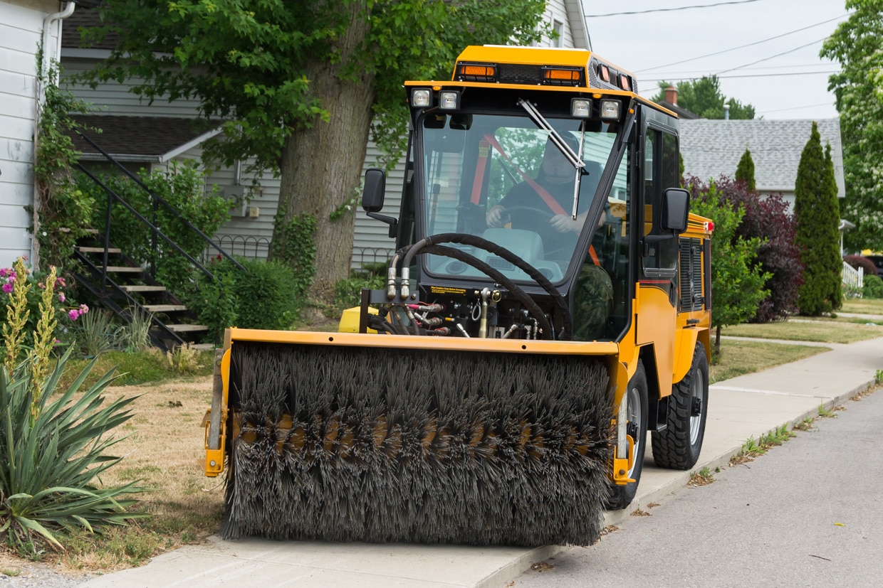 trackless vehicles power angle sweeper attachment on sidewalk municipal tractor working on sidewalk front view